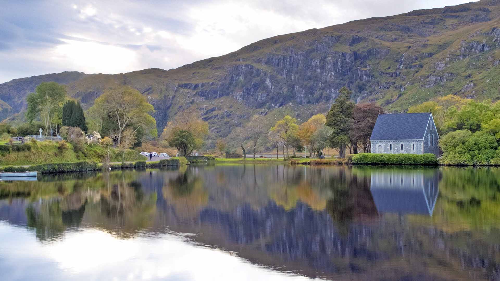 a lake with a Gougane Barra Church and mountains in the background