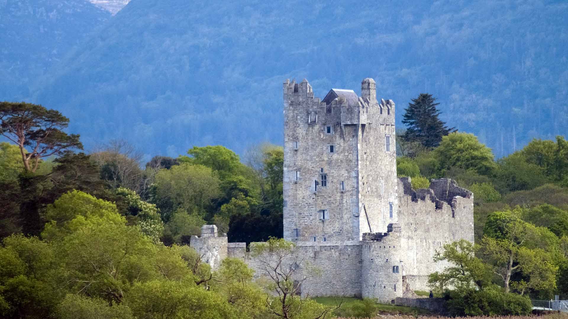 a stone castle with trees and mountains in the background