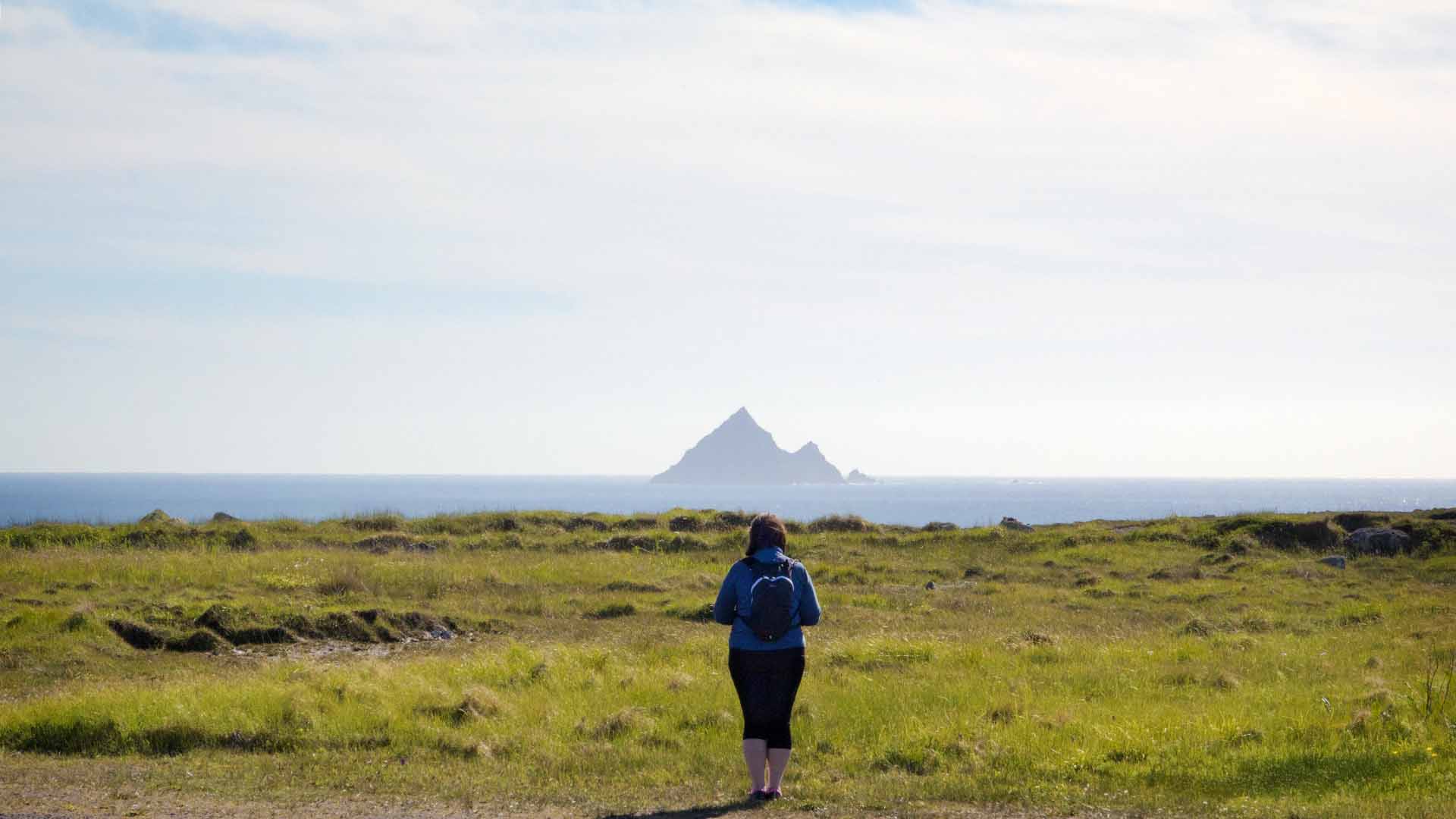 a woman standing in a field with a small island in the distance