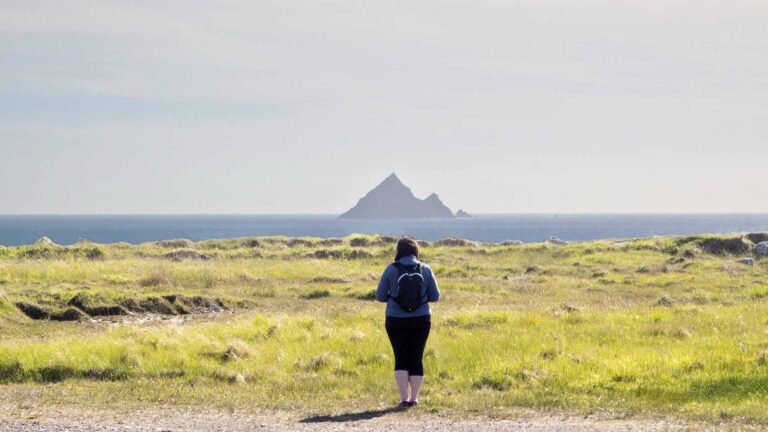 a woman standing in a field with a small island in the distance