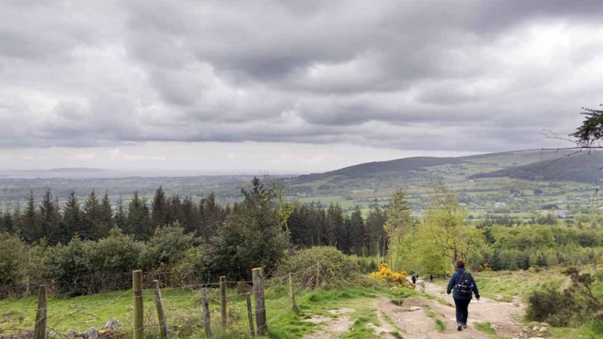 a person walking on a path with trees and mountains in the background Hell Fire Club